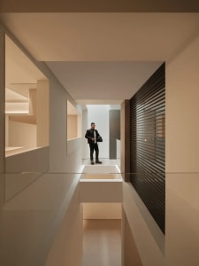 A man stands in a modern room with a white wall, glass wall, and black and white color scheme, creating a calm and serene atmosphere