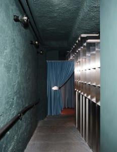 A calm and inviting hallway with a blue and white curtain hanging in front of a doorway, surrounded by stone walls and a metal railing
