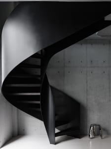A black and white photo of a spiral metal staircase in a dimly lit room with a metal trash can at the base