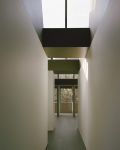 Narrow hallway with a vaulted ceiling, white walls, and natural light from unknown sources