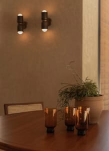 A modern living room with a wooden dining table, four candles in glass vases, and a potted plant, surrounded by clean lines and minimalistic decor