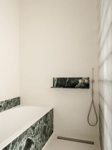 Modern bathroom with a white bathtub, shower, and marble countertop, set in a dimly lit space with clean lines and minimalistic design elements