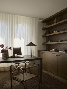 A modern study with a desk, chair, and bookshelf, featuring a lamp on the desk and a well-lit, organized space
