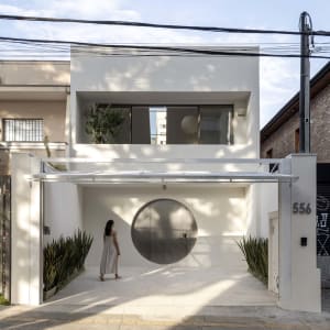 A modern white house with a circular window on the front, surrounded by a well-maintained garden