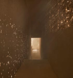 A simple functional hallway with concrete walls, lights on the wall, and a doorway leading to another room, creating a warm and inviting atmosphere