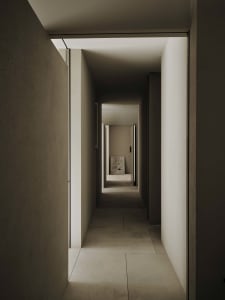 Narrow hallway with a stone floor, a chair, and a cat, in a dimly lit space with a white color scheme