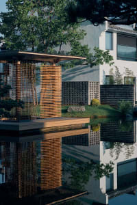 A serene outdoor living space with a white building, wooden deck, stone wall, and small pond in a garden-like setting