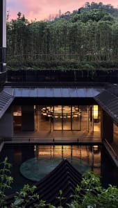 A dimly lit modern room with a pool in the center, surrounded by furniture and decorated with wood and glass materials