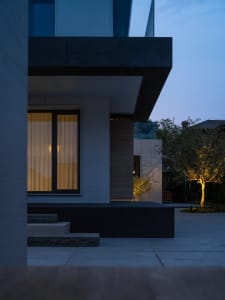 A modern house with a black and white color scheme and a large window, set at night with the house's lights illuminating the area