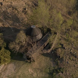 A serene image of a dome-shaped building surrounded by trees, with a black dome contrasting with the green surroundings, set against a sunny day