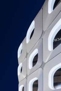 A modern office building with a white facade and a large glass window, illuminated by natural light