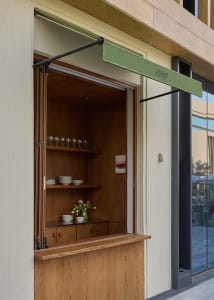 Modern kitchen with a wooden counter, display of plates and bowls, and wine glasses, with a view of the interior through an open door