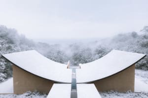 A modern building with a curved structure is set against a serene snow-covered landscape