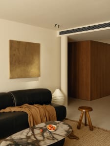 Cozy living room with a black couch, chair, and dining table, featuring a white wall, brown wooden door, and decorative elements