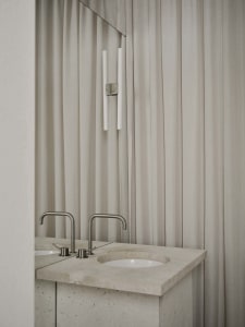 Bathroom with a marble sink under a white curtain, a mirror above, and a white color scheme, lit by natural light