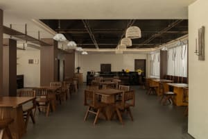 A modern restaurant with a large dining area featuring wooden tables and chairs, well-lit to create a warm and inviting atmosphere