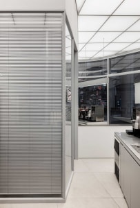 A clean and organized kitchen with a gray wall, a window, and a countertop with cups and a bowl in various positions