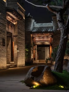 A traditional Chinese building with a stone facade, featuring a large archway and a stone-paved courtyard, under dim lighting