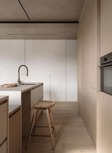 A modern kitchen with wooden cabinets, a white countertop, and a dining table, featuring a sink, stove, and refrigerator, with a dimly lit atmosphere