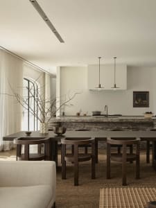 Modern kitchen with a marble countertop, wooden floor, and natural light from windows, featuring a center island and dining area