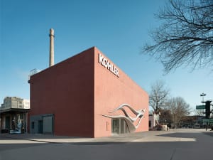 A modern building with a red brick exterior, a white sign, and a street in the background, set in a bright and inviting urban environment