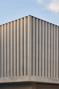 Photograph of a modern building with a white concrete facade, featuring a row of vertical windows and natural light from above