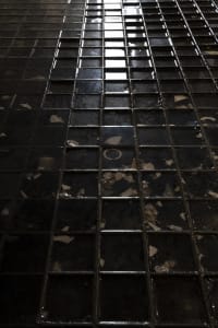 A dimly lit black and white photograph of a tile floor, possibly in a bathroom, with a minimalist and functional style
