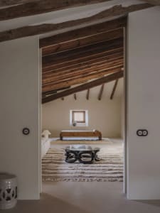 Cozy living room with a wooden floor, a white wall, a couch, a chair, and a dining table, with natural lighting and wooden elements creating a warm and comfortable space