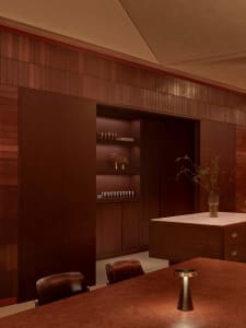 A warm and inviting living space with wooden walls and floor, featuring a wooden table, chair, cabinet, and potted plant