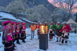 A group of people gathered around a fire pit in a snowy outdoor setting, surrounded by trees and natural scenery