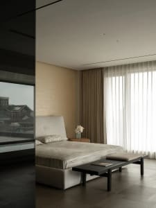 A well-lit bedroom with a bed, bench, and window, featuring predominantly white materials and a cozy atmosphere