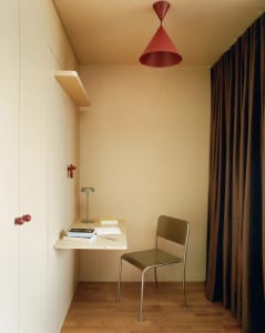 A small, dimly lit room with a brown chair and table, and a red light hanging from the ceiling