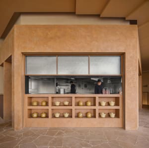 A casual restaurant kitchen with a wooden counter, natural light, and two people preparing or enjoying a meal
