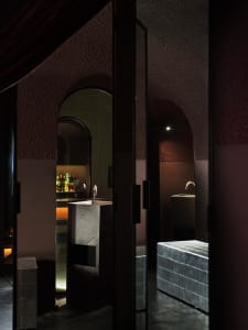 Bathroom with a stone-like appearance, featuring a sink, mirror, and shower, with dim lighting creating a cozy atmosphere