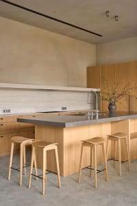 A modern kitchen with wooden cabinets, a marble countertop, and wooden stools, featuring a gray countertop and warm lighting