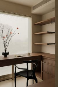 Cozy home office with a wooden desk, a black chair, and a vase with flowers on a natural light-filled room