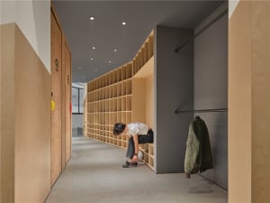 A person sits on a step in a hallway lined with wooden shelves and doors, creating a calm and inviting atmosphere