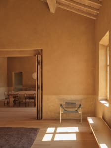 Cozy dining space with a wooden floor, a dining table, chairs, and a bench, surrounded by cement walls and natural light from a window