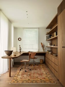 Small office space with a wooden desk, brown chair, and bookshelf, natural light from a window