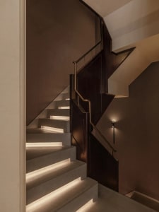 A wooden staircase with a metal railing in a well-lit hallway, captured from a perspective looking up the stairs