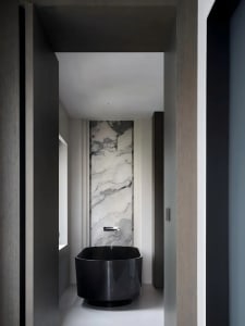 Black and white photograph of a modern bathroom with a black bathtub, toilet, and sink, set against a backdrop of marble walls in a dimly lit space