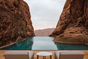 A serene outdoor patio with a pool surrounded by a rock wall, featuring two couches and a dining table