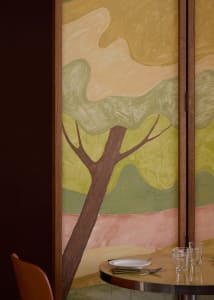 Impressionist painting of a tree in a forest, set in a brown wooden frame, with warm and inviting lighting