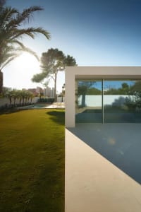 A serene white house with a glass wall surrounded by a lush green field, allowing natural light to enter and creating a bright and inviting space