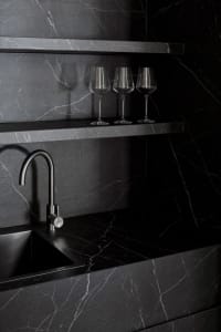 A modern kitchen with a marble counter, sink, and three wine glasses, set in a dimly lit space