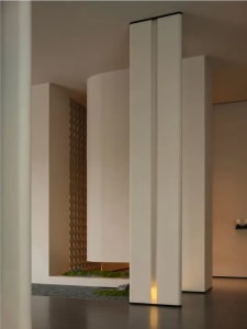 A large, open room with a white color scheme, white pillars, and a small garden area with a potted plant, creating a clean and minimalistic atmosphere