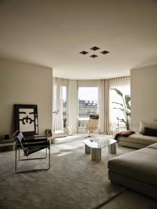 A well-lit living room with a couch, chair, and glass table, furnished with a potted plant, vase, and book, creating a modern and inviting space for relaxation and socializing