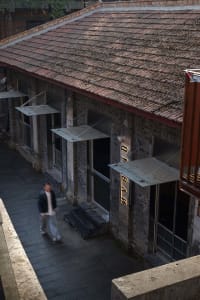 A brick building with a red roof and a man walking in front of it, set in an urban environment with a mix of architectural styles