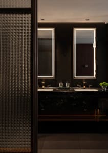A dimly lit bathroom with a sink, mirror, and toilet, featuring marble countertops and a classic, functional design