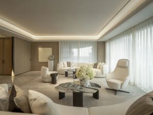 A modern living room with a glass window, natural light, and a variety of seating options, including couches, chairs, and a bench, with a dining table and a vase of flowers